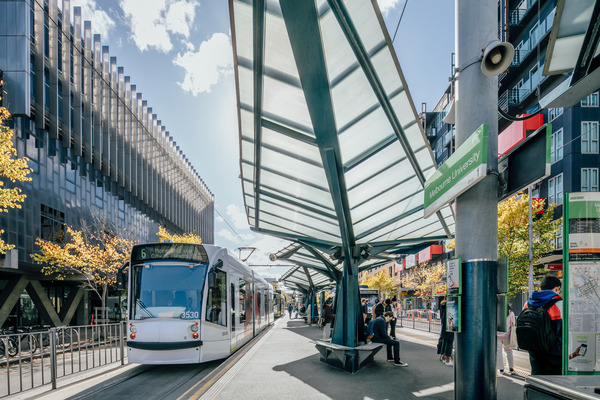 Tram arriving at tram stop, people waiting and sitting
