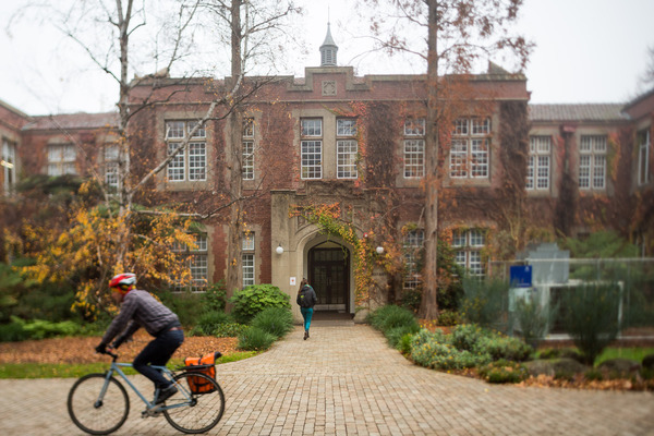 Man rides bike passed brick building covered in vines.