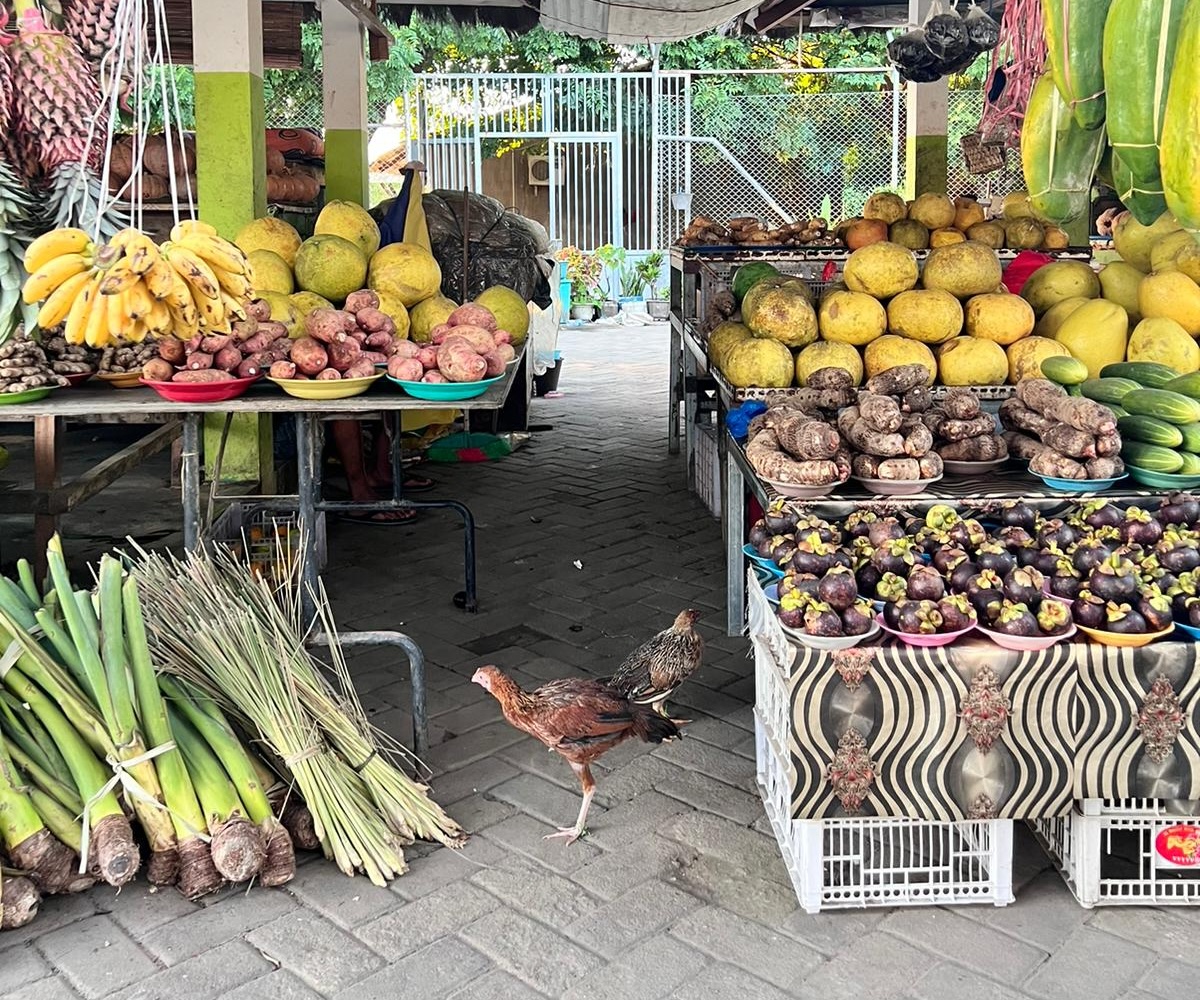 A food market filled with all kinds of fruits and vegetables, with a chicken standing in the middle of it